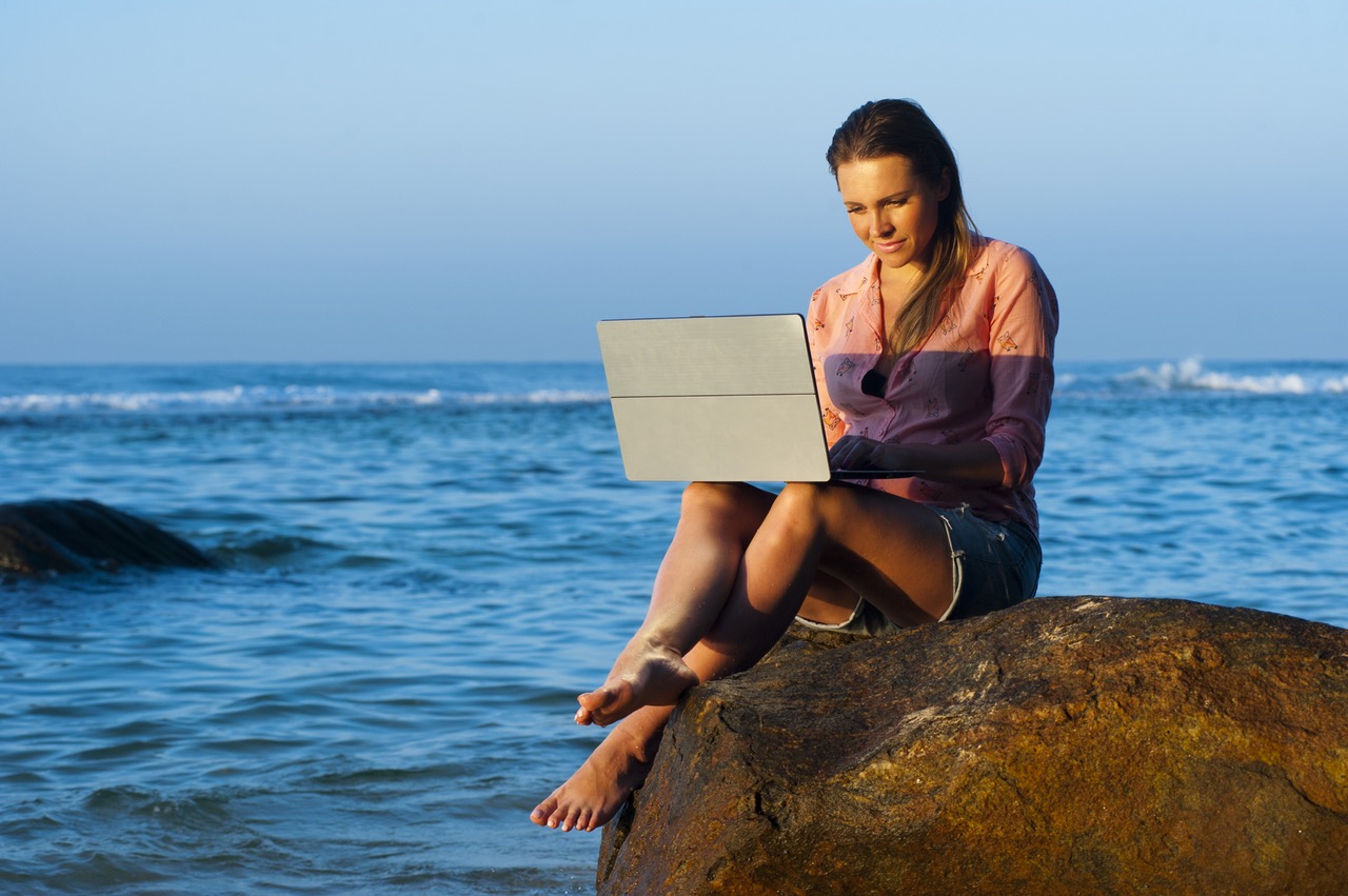 Lady uses laptop on the beach - Credits to https://costculator.com/