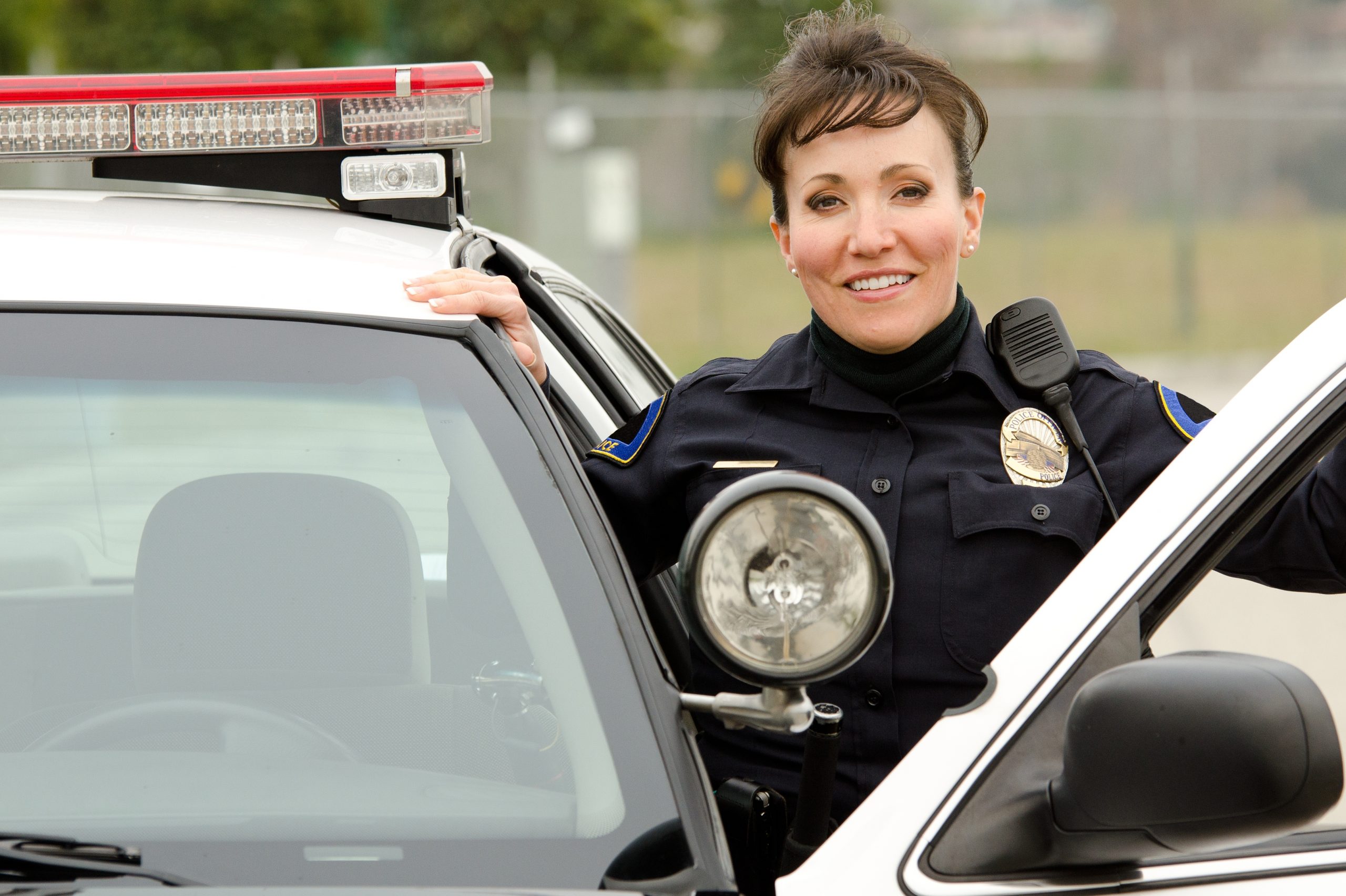 Woman police officer smiles at police car