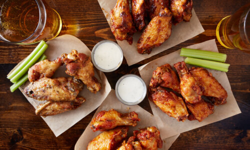 overhead view of four different flavored chicken wings with ranch dressing, beer, and celery sticks
