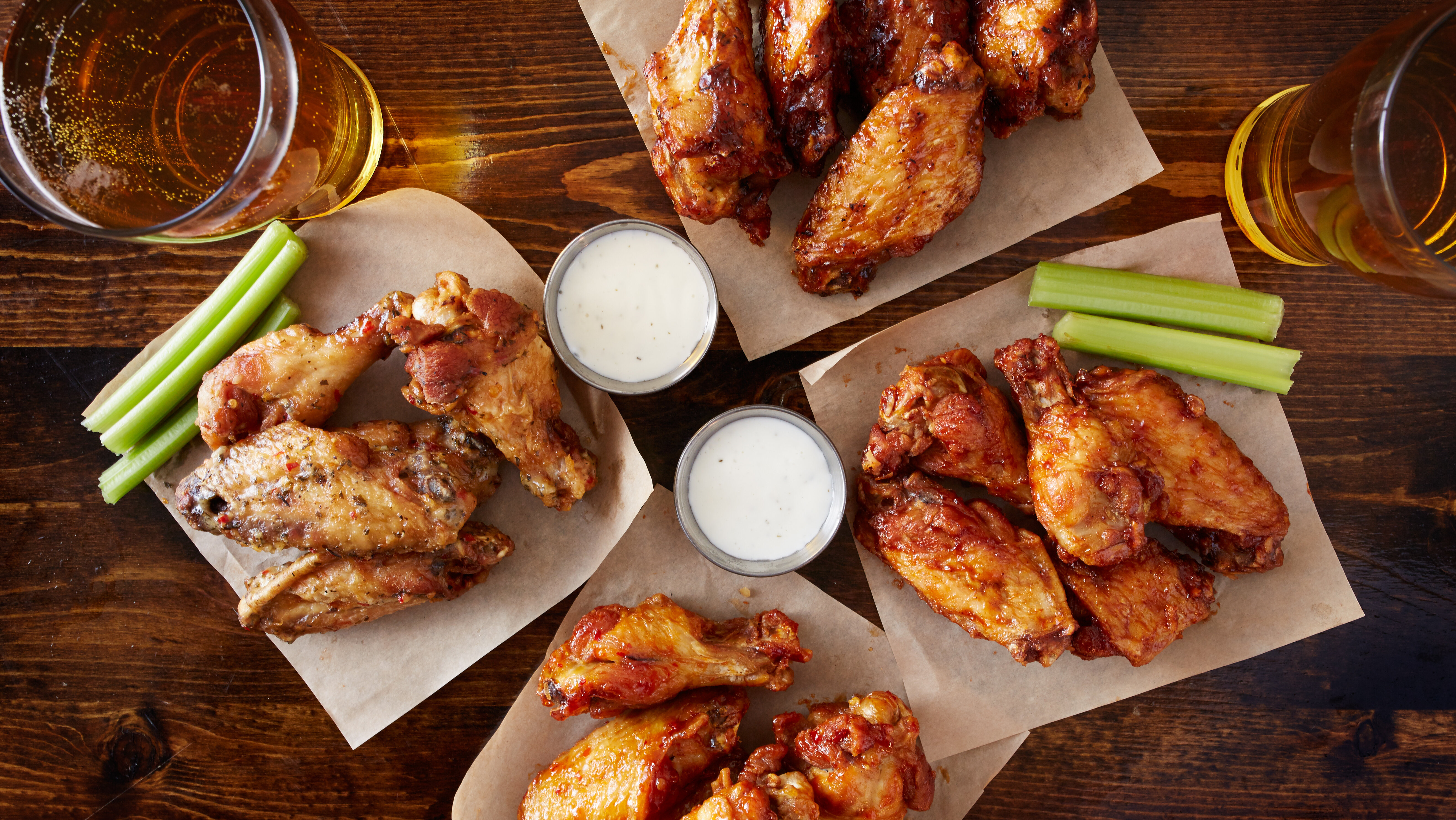 overhead view of four different flavored chicken wings with ranch dressing, beer, and celery sticks
