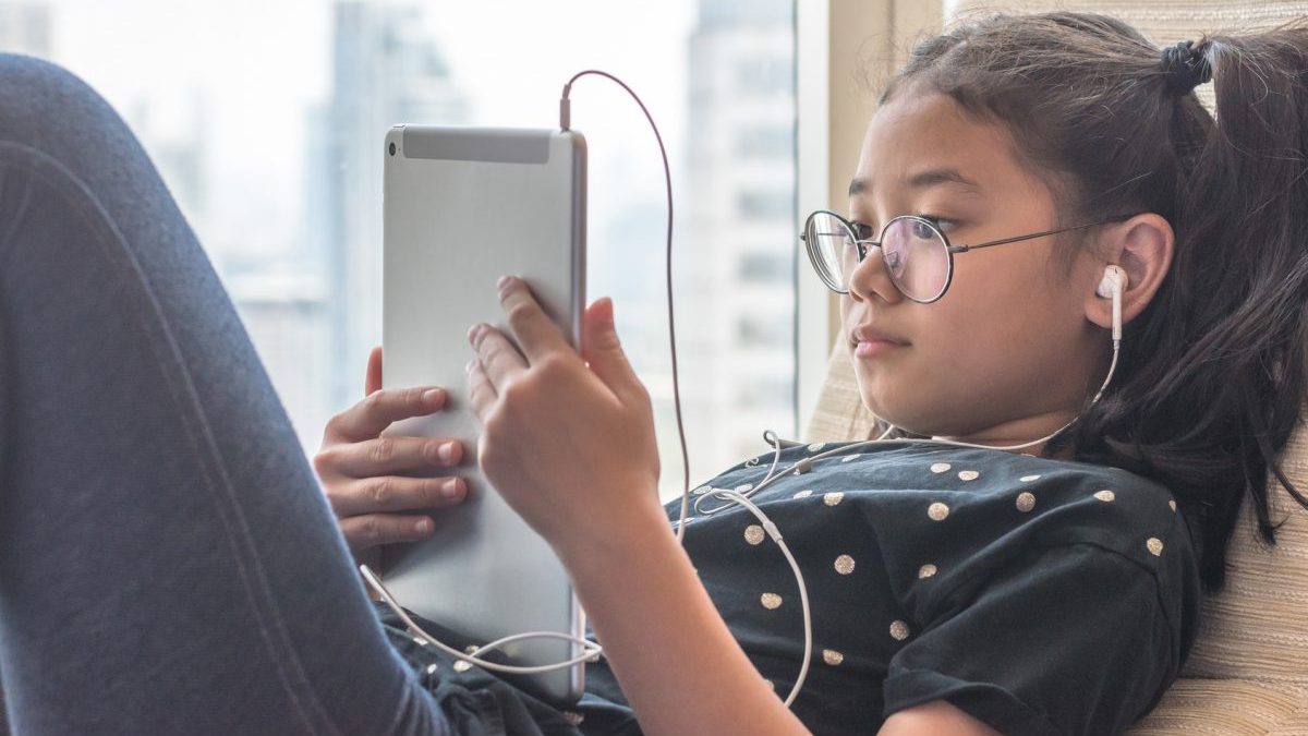 child reclining using an iPad and corded ear buds
