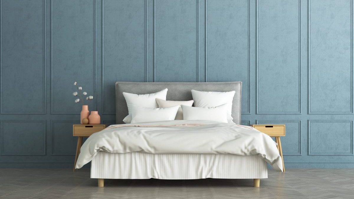 A neatly made bed with a bed skirt is shown against a pale blue wall.
