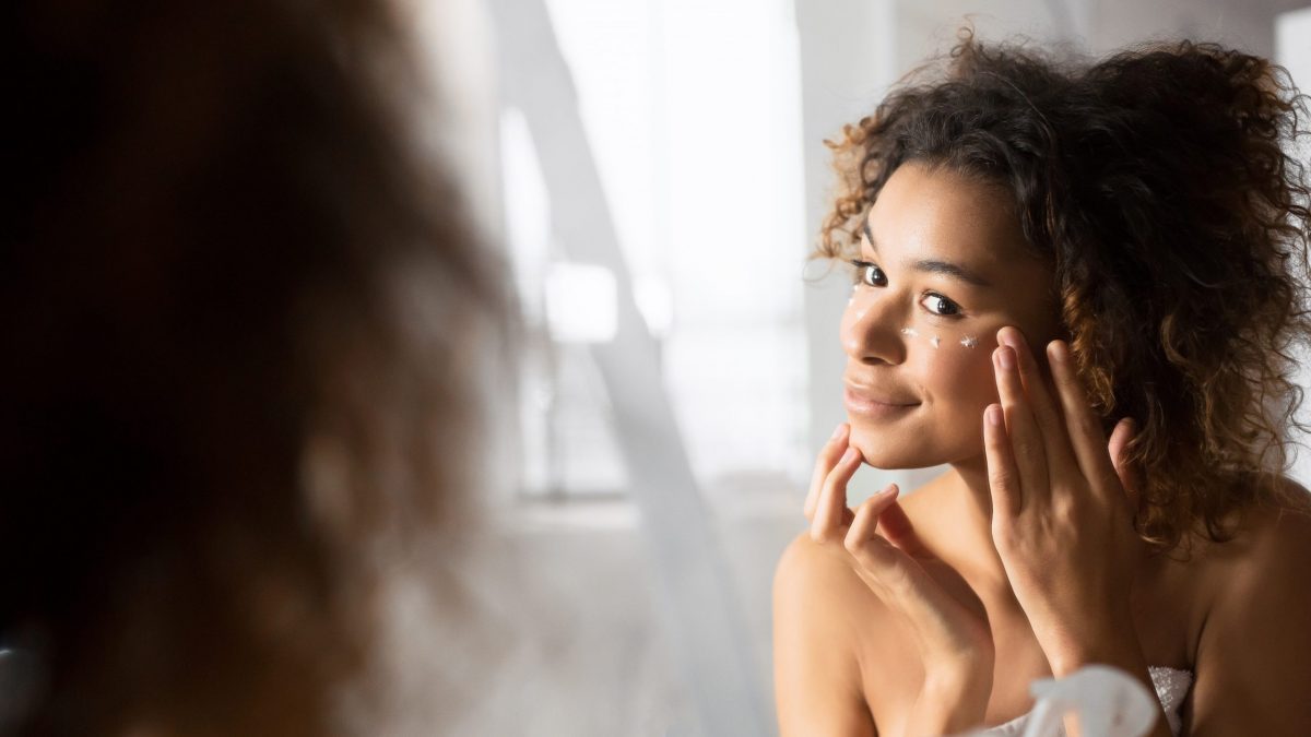 Woman looks in mirror to apply eye cream
