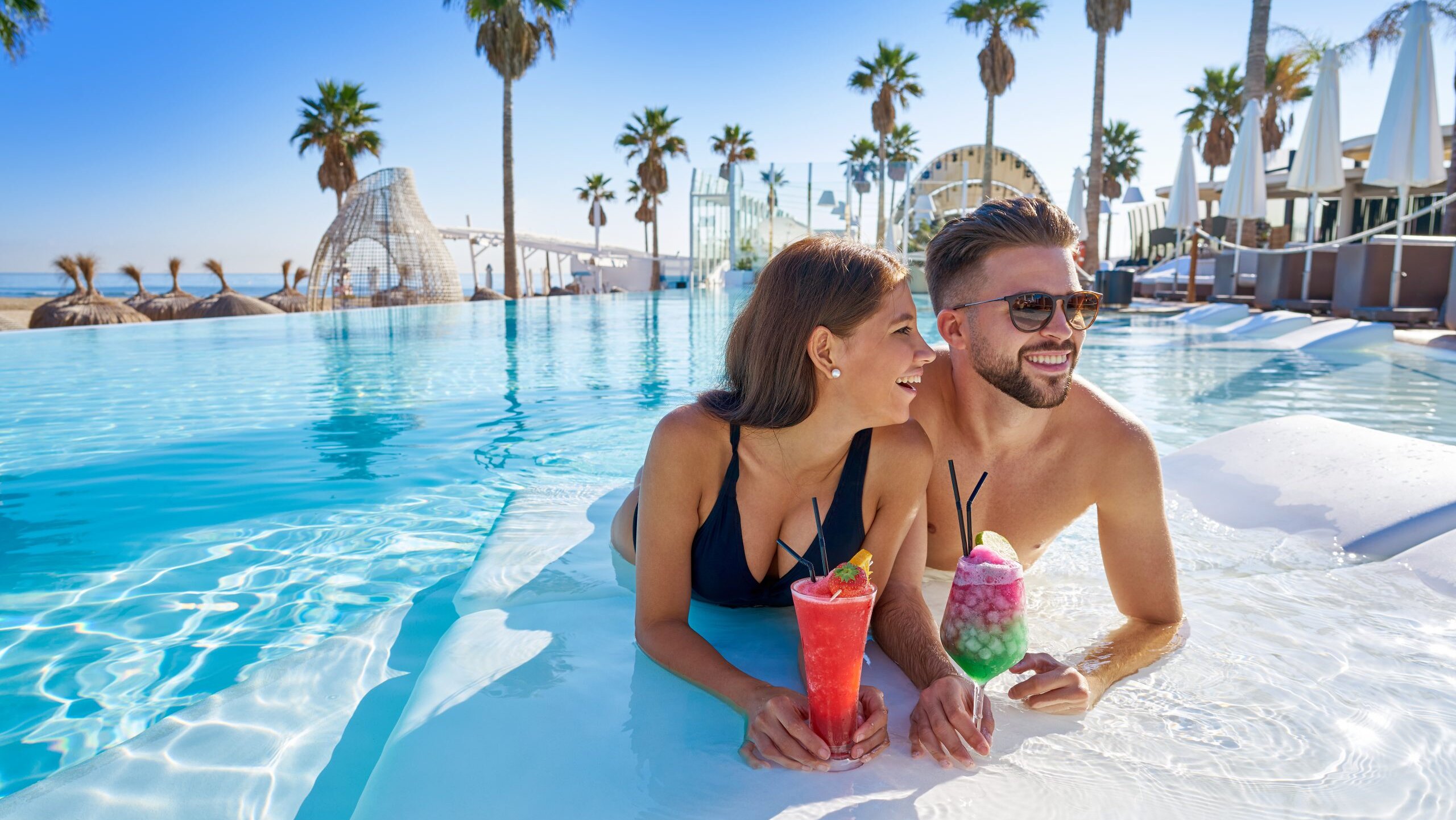 Young couple enjoys vacation in pool with cocktails