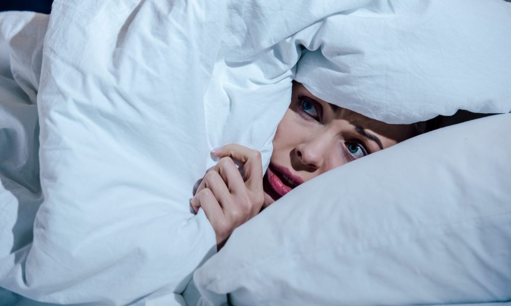 Scared woman hides behind blanket