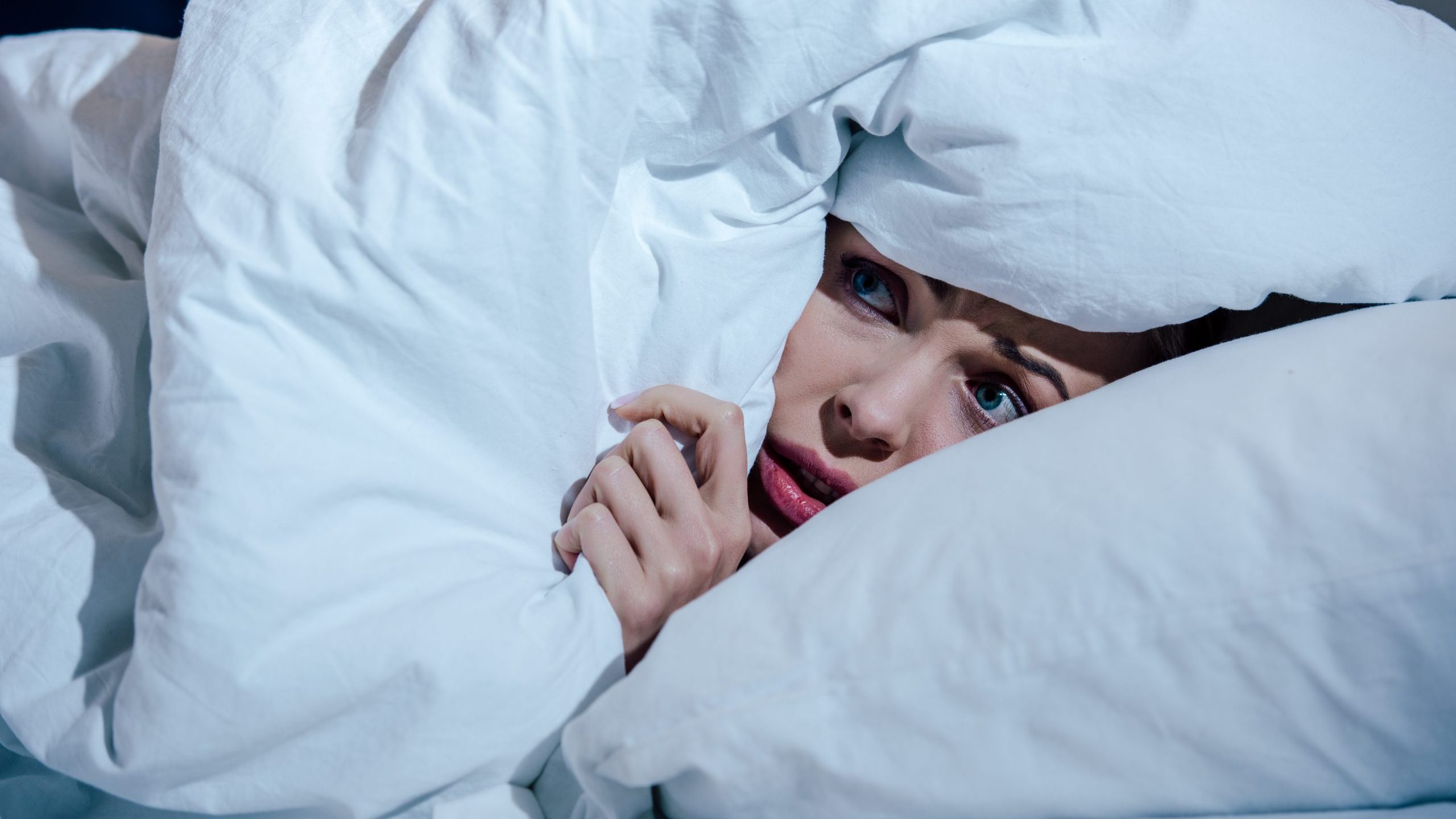 Scared woman hides behind blanket