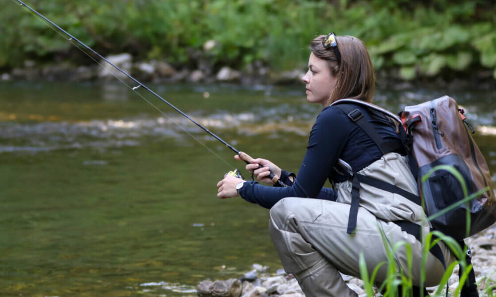 woman crouches by river to fish