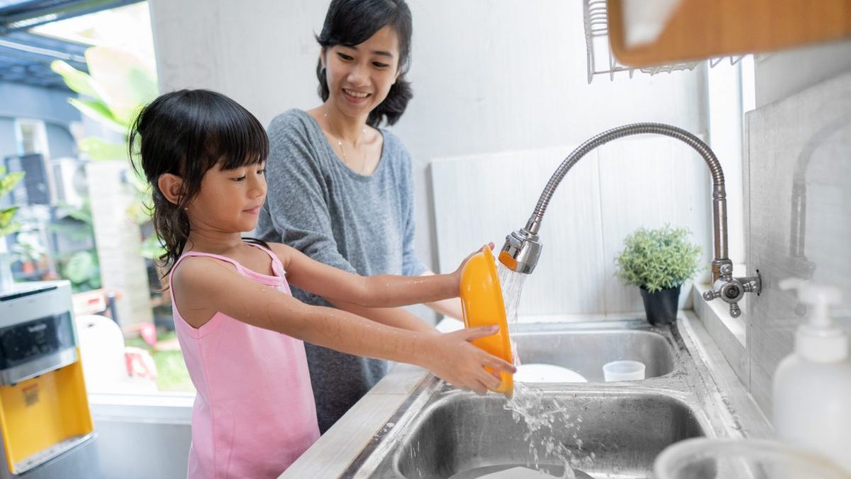 A girl helps her mom do dishes in a double kitchen sink.
