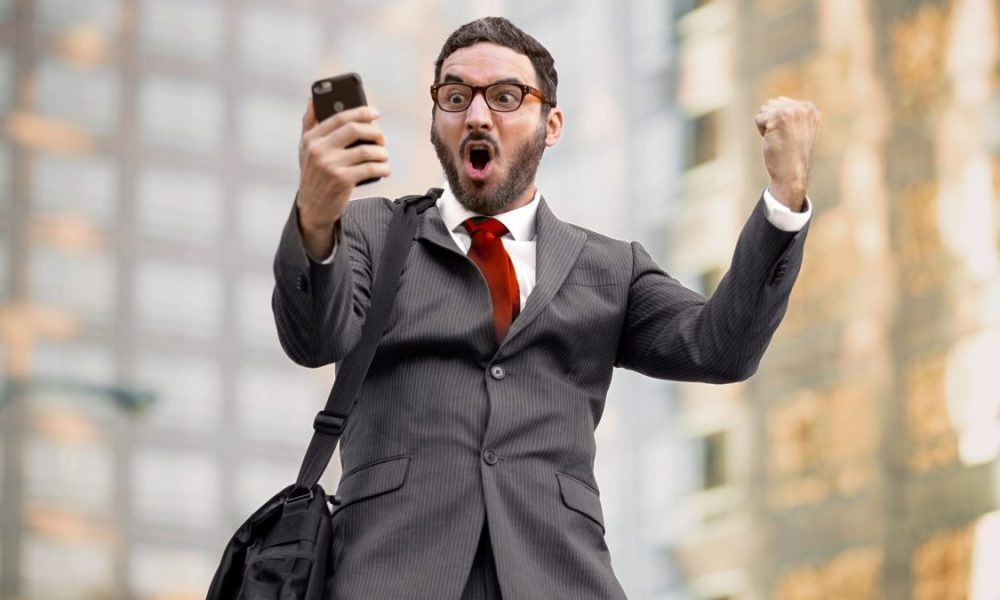 Man in suit looks at his phone, screams in excitement.