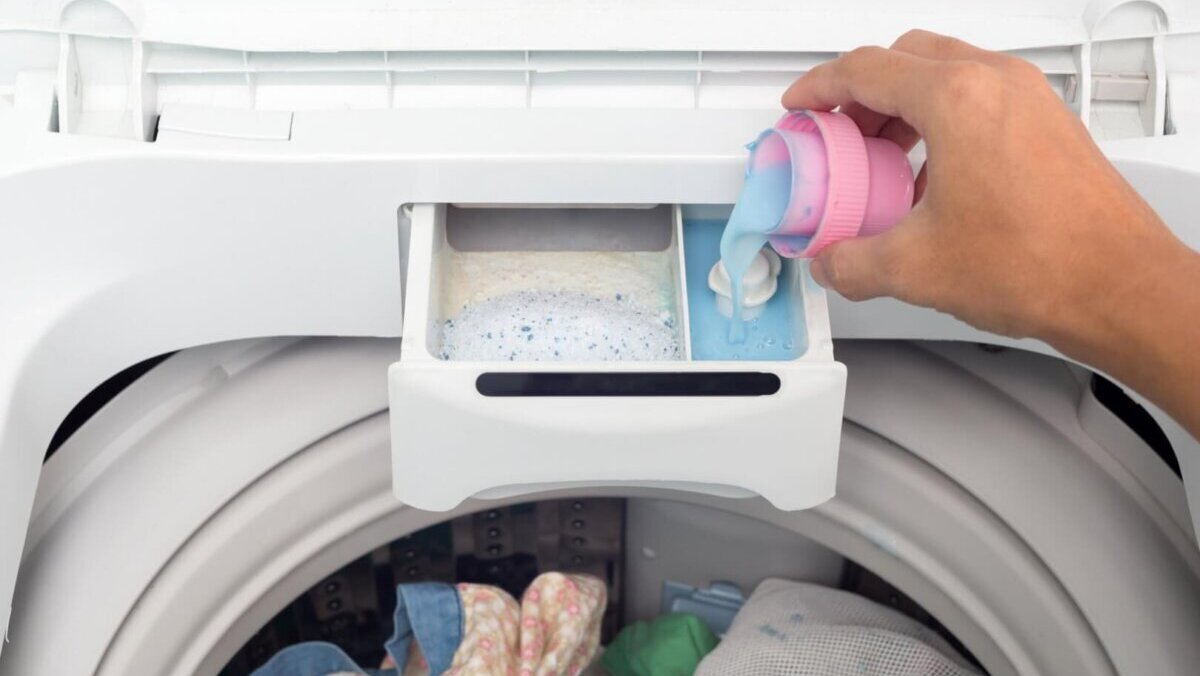 a hand pours fabric softener into washing machine