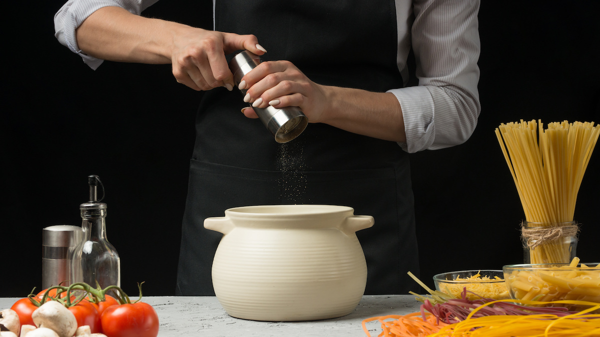 Chef using a pepper grinder over a bowl.