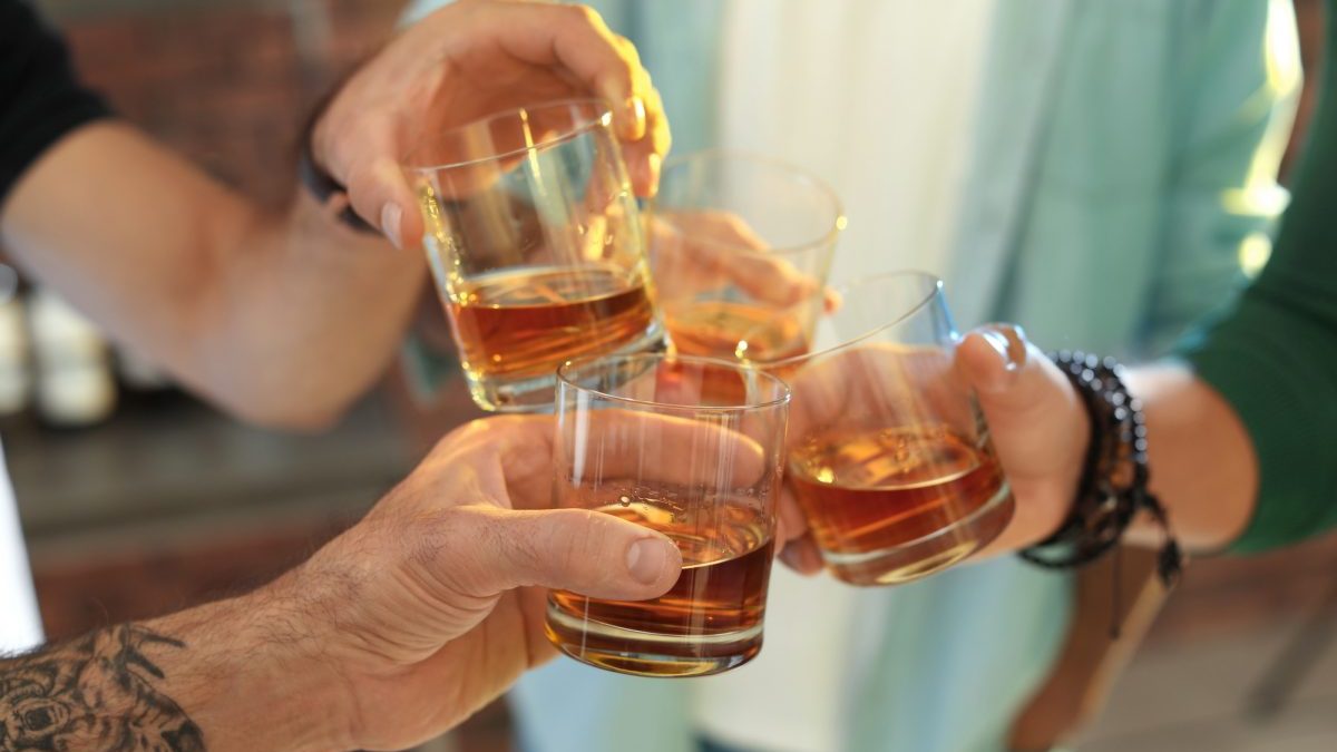 Friends toasting with glasses of whiskey indoors, closeup