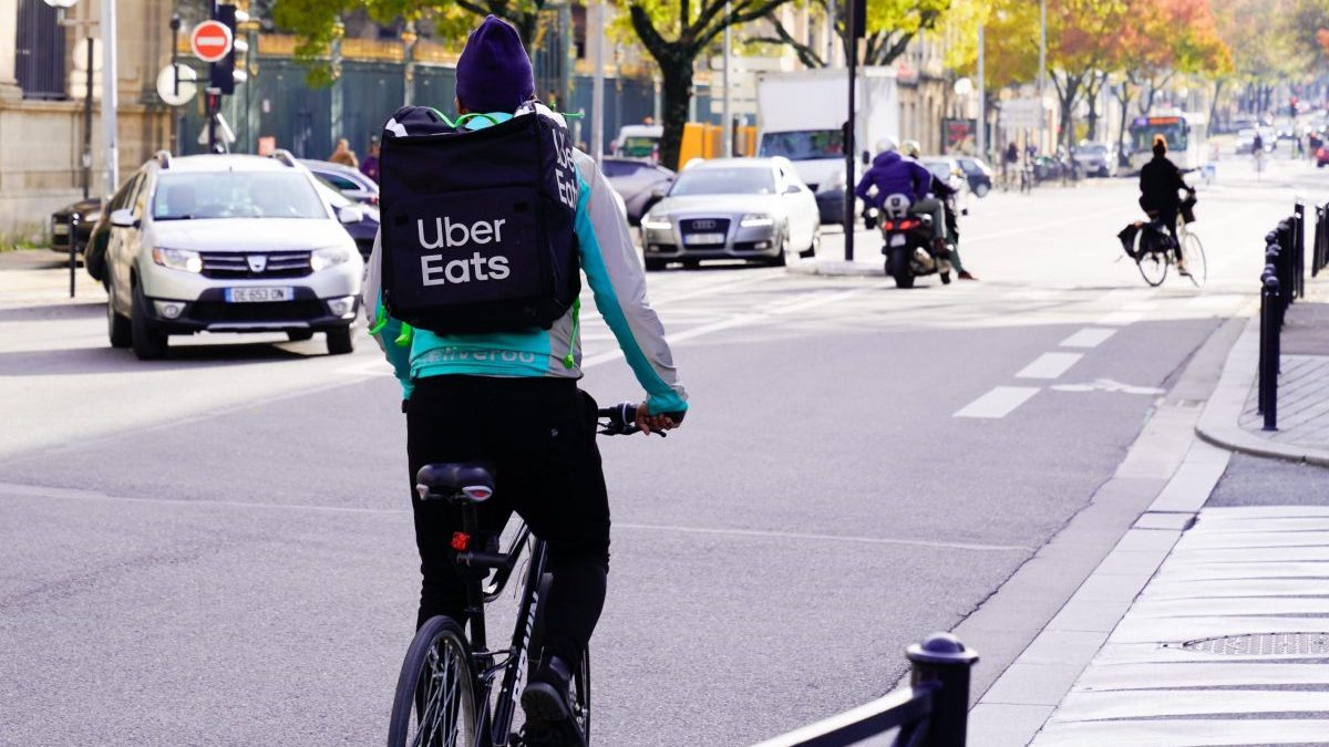 An Uber Eats delivery person rides a bike with the company's logo on their backpack.