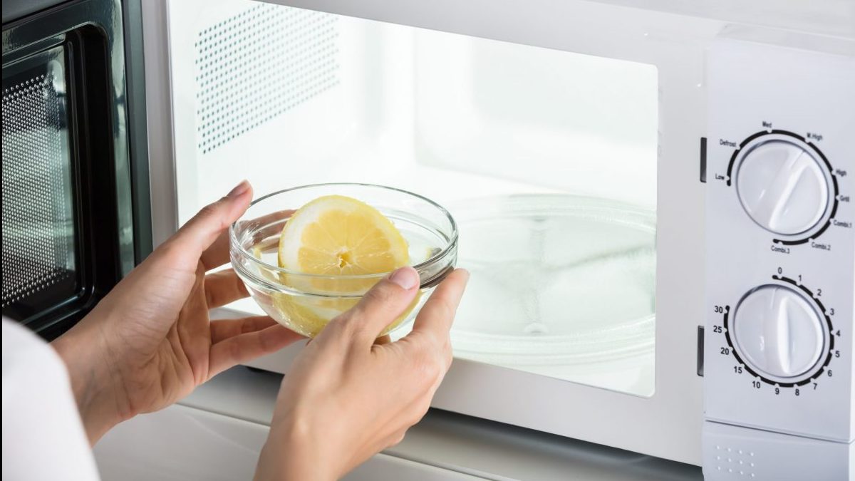 Woman Putting Bowl Of Slice Lemon In Microwave Oven to clean it.