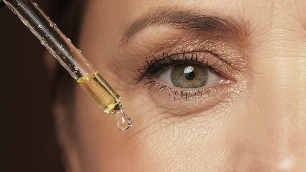 Woman uses vitamin C serum below eye for skin care.