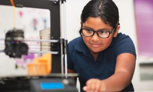 A young girl uses a 3D printer to make a model at school.