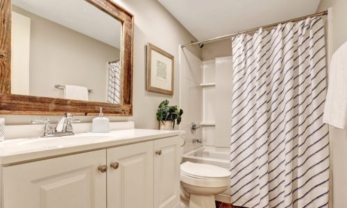 A white bathroom with a framed mirror and patterned shower curtain.
