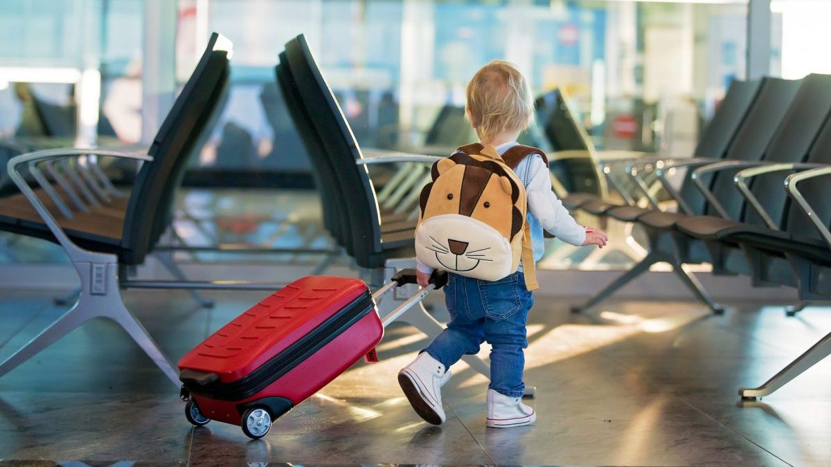 A young child wheels their suitcase through an airport terminal.