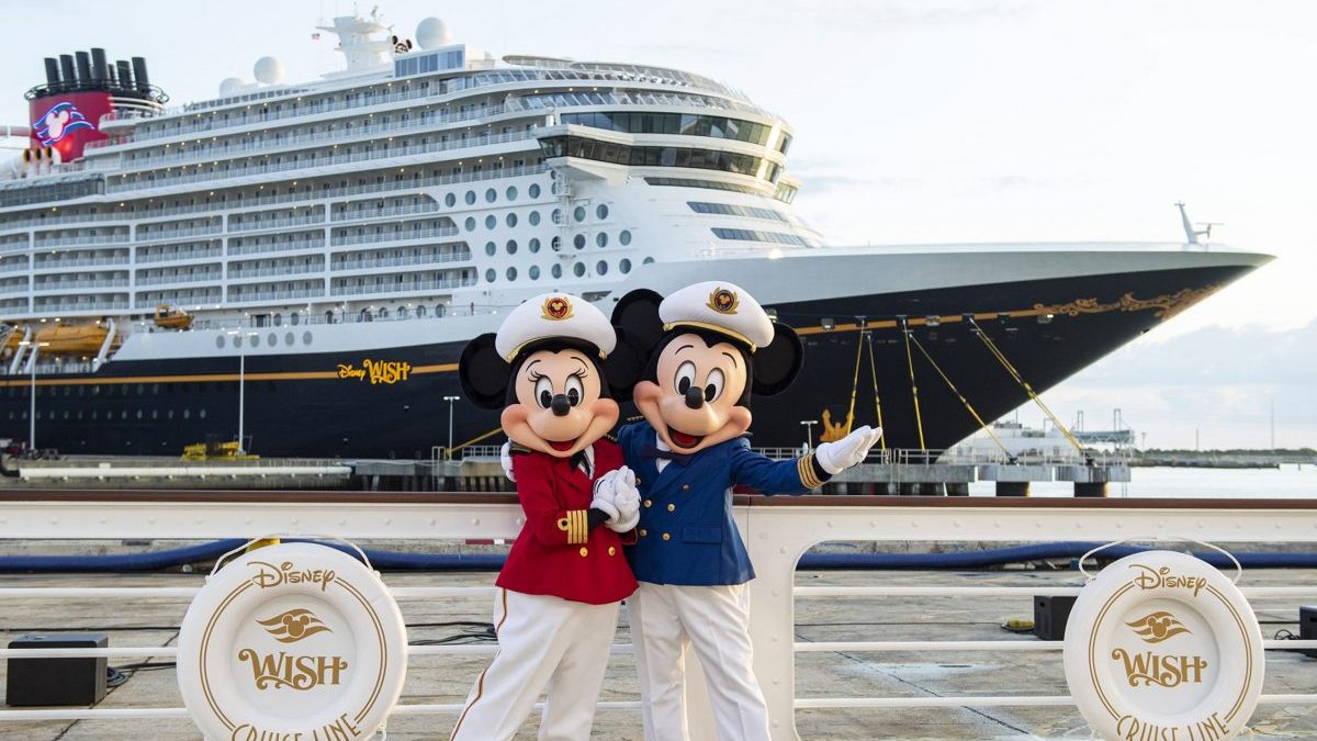 Minnie and Mickey Mouse stand in front of the Disney Wish cruise ship.