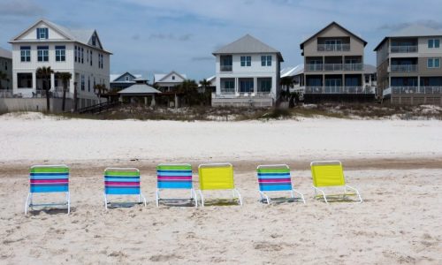 A row of beach chairs on a sandy beach in front of vacation rental houses.