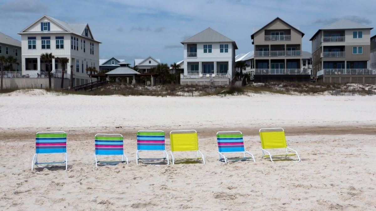 A row of beach chairs on a sandy beach in front of vacation rental houses.