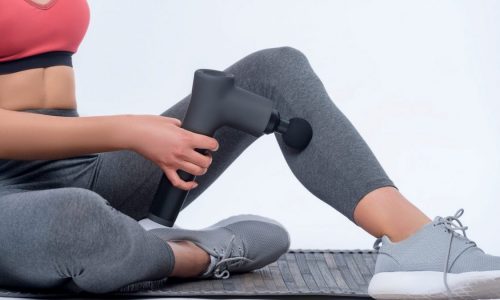 A woman uses a handheld massage fun on her calf after a workout.