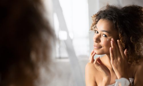 woman putting on eye cream in mirror