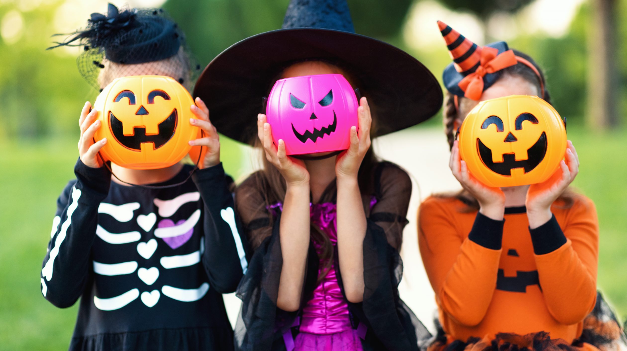 Kids in cute Halloween costumes hold candy buckets
