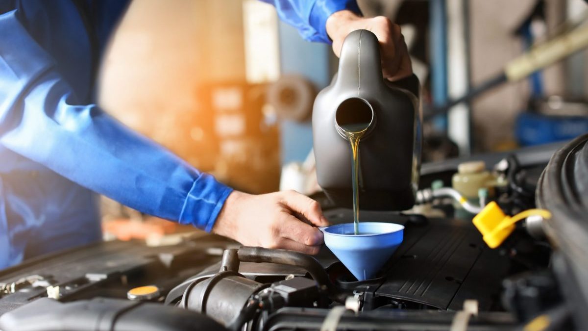 Male mechanic refilling car oil in service center.