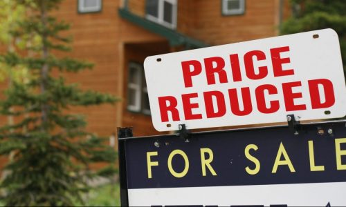 A "Price Reduced" notice is seen on a home's "For Sale" sign in the yard.