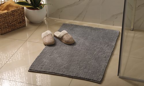 Soft grey bath mat and slippers on floor in bathroom