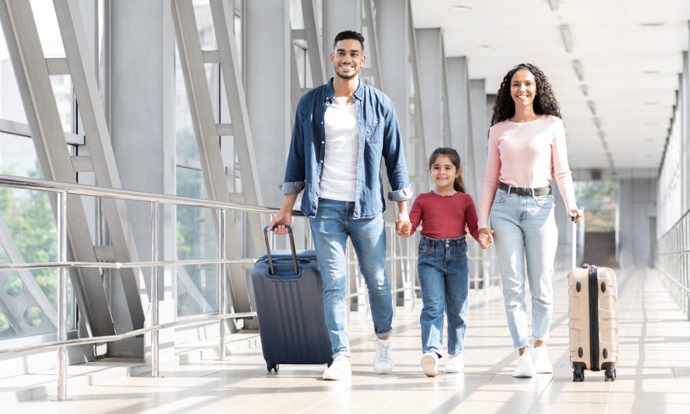 Family walks in airport terminal with suitcases
