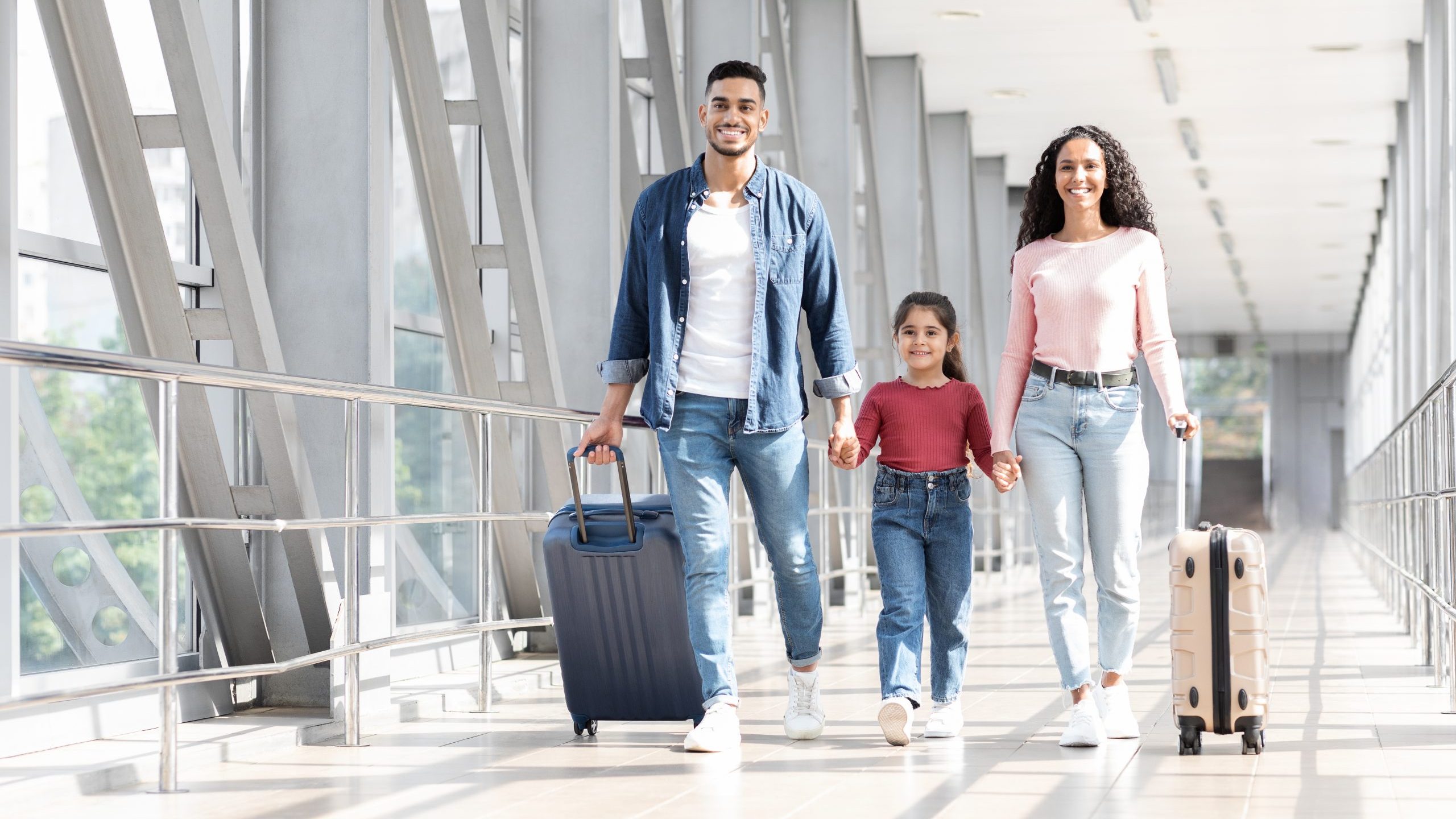 Family walks in airport terminal with suitcases