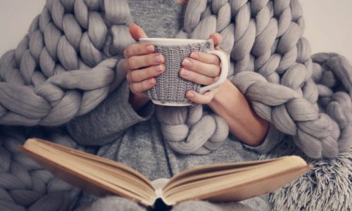 Cozy Woman covered with warm soft merino wool blanket reading a book.