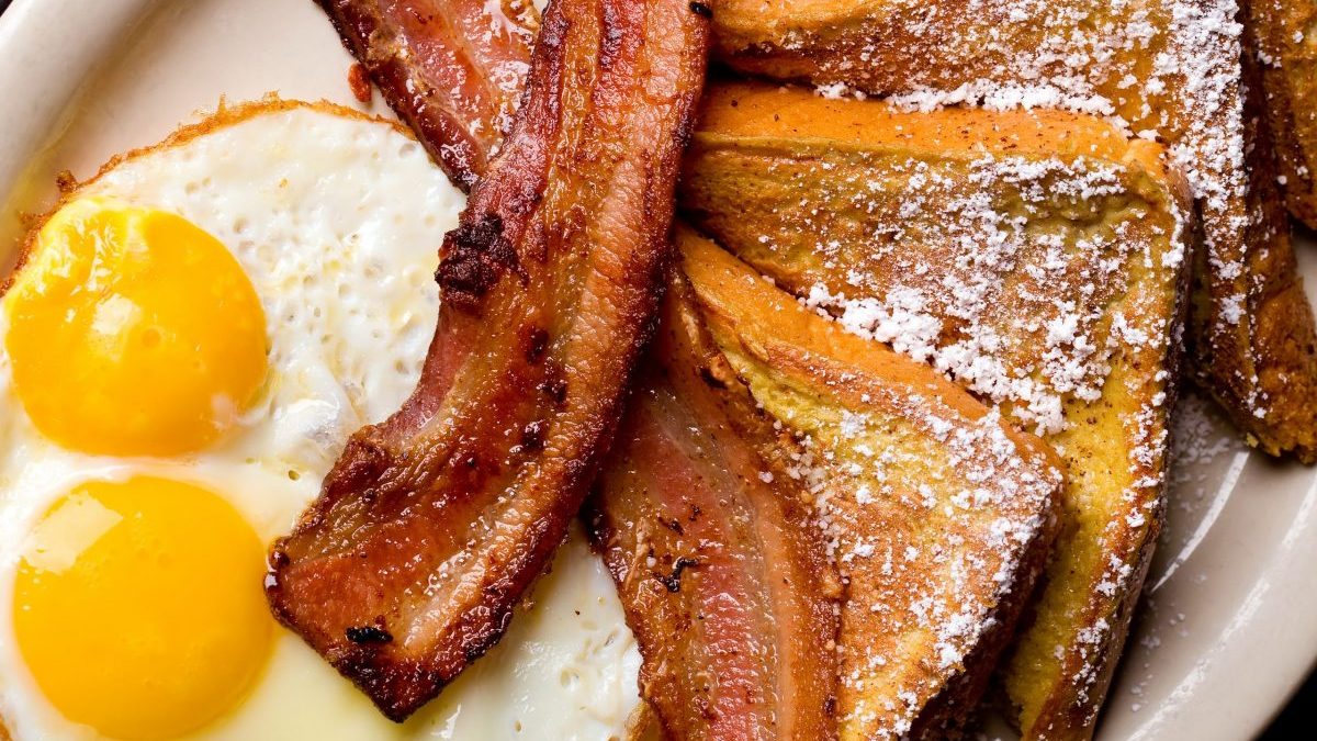 A diner breakfast of French toast, bacon and eggs over easy is shown.