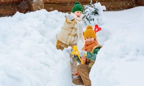 Two happy family kids playing snowballs among the snowdrifts. Winter active games for kids. Kids dressed in warm colored knitted retro clothes.