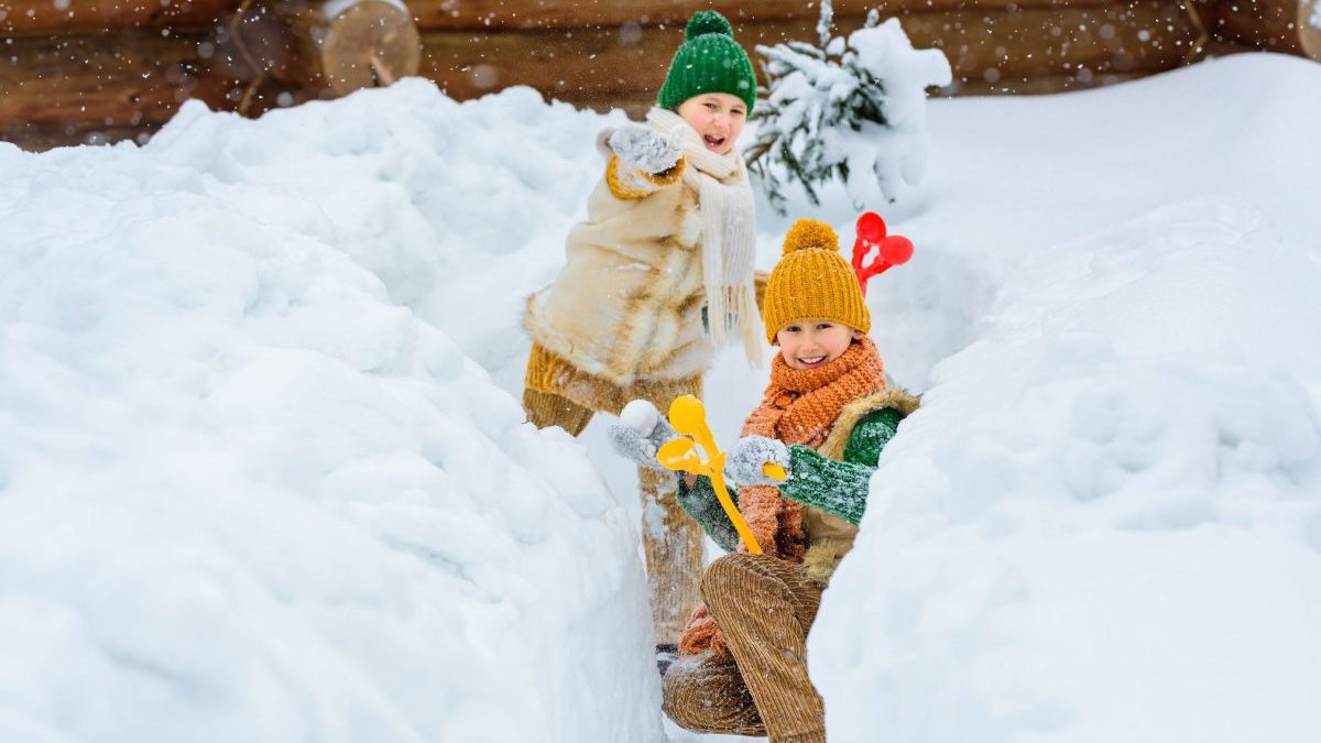 Two happy family kids playing snowballs among the snowdrifts. Winter active games for kids. Kids dressed in warm colored knitted retro clothes.