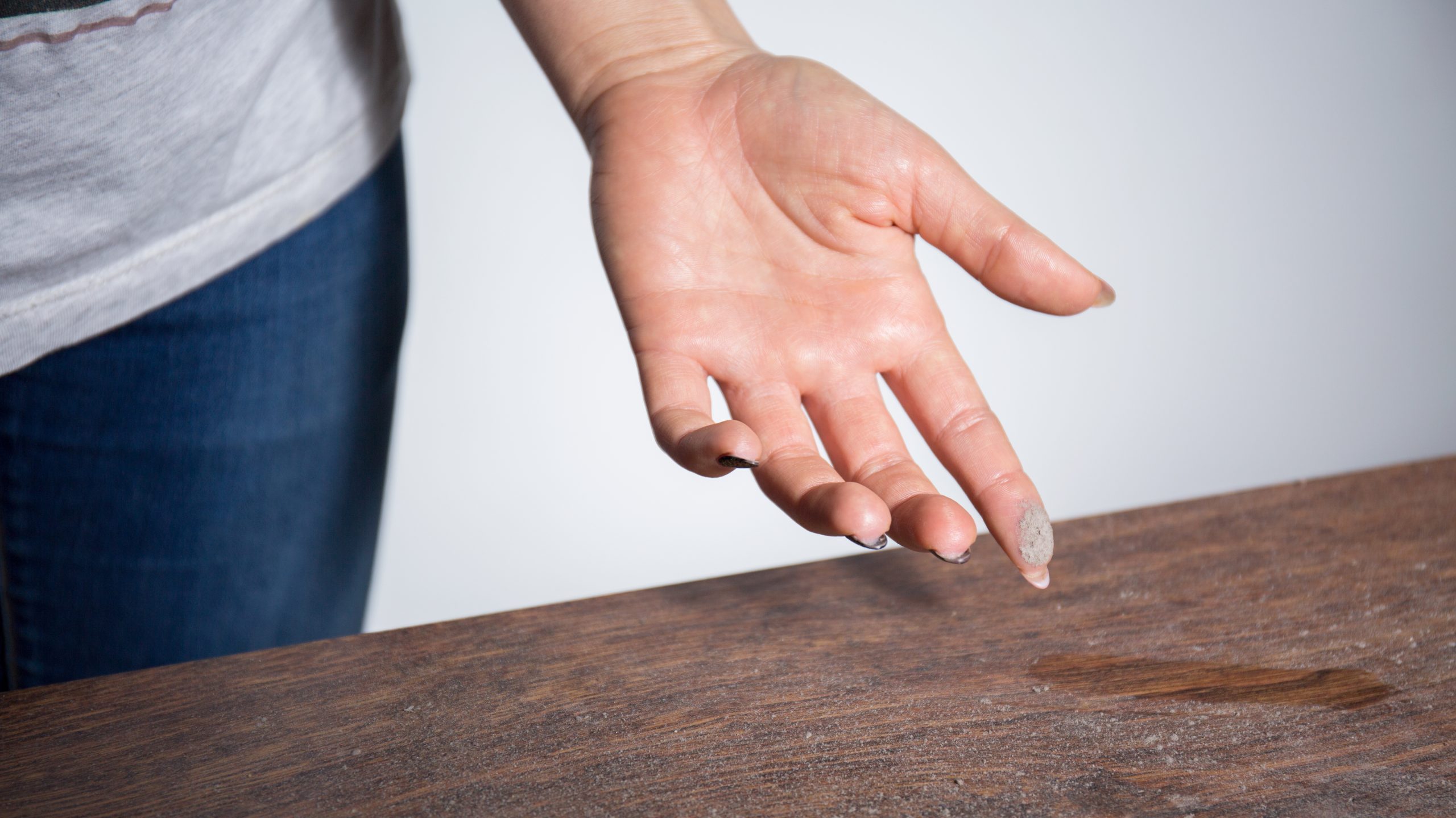 Woman swipes up dust on furniture with finger
