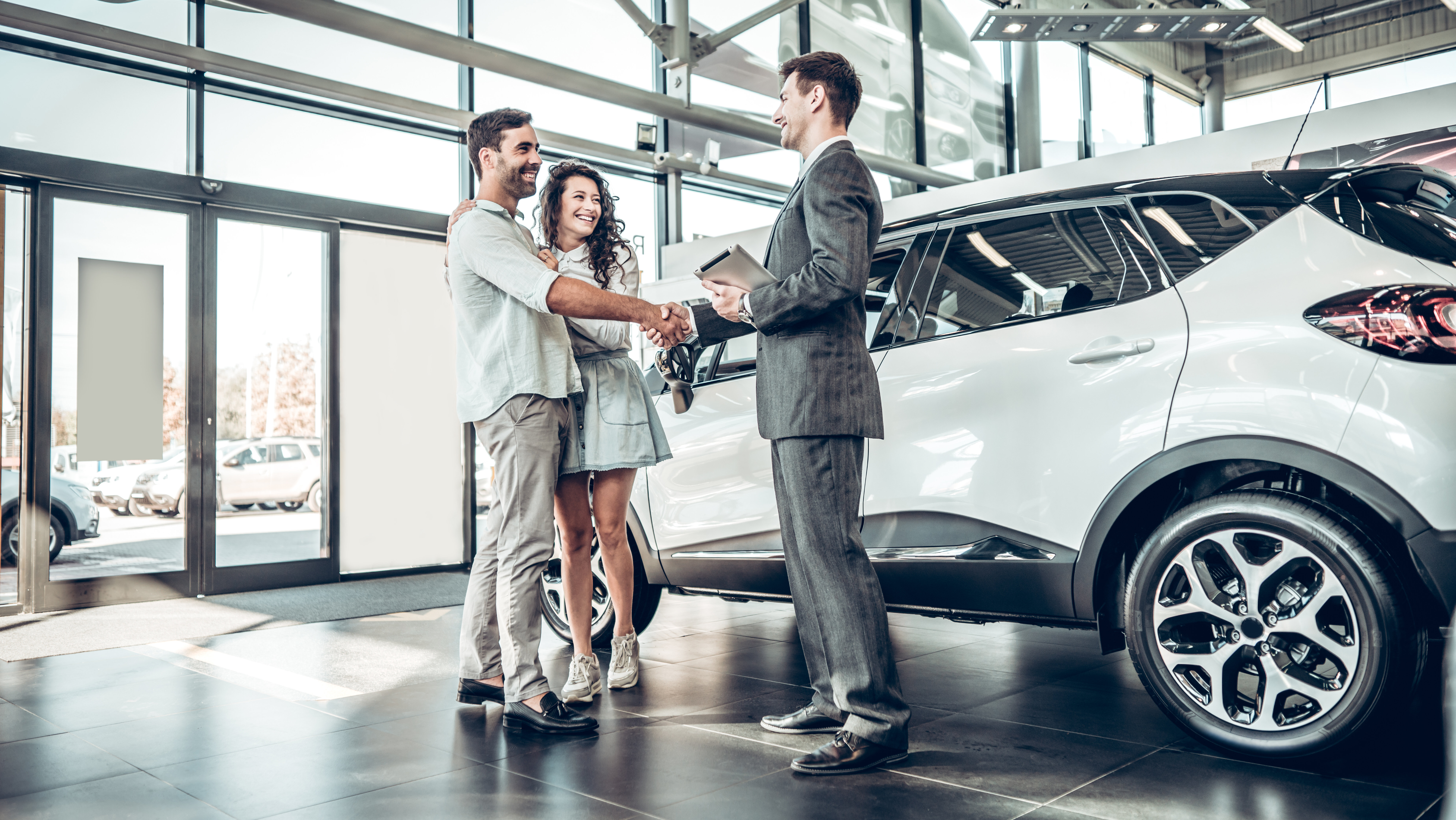 Young couple in a car dealership shaking hands with sales agent