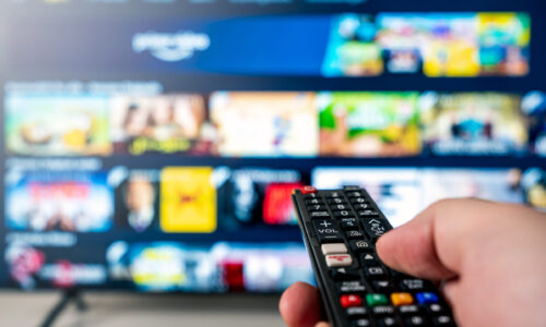 Hand holds remote choosing from many streaming options on TV