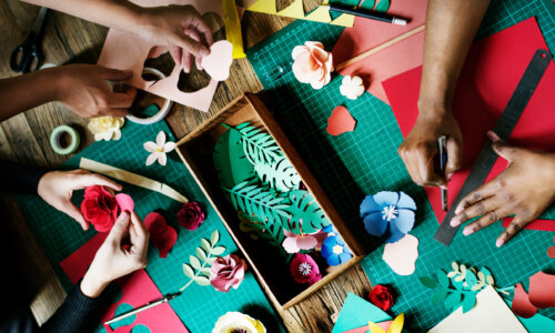 Hands make crafts and table with paper cutouts, ribbon and tape