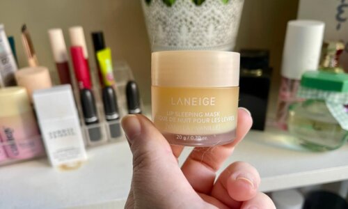 Commerce editor Shea Simmons holds up the Laneige Lip Sleeping Mask in vanilla in front of a shelf of makeup.