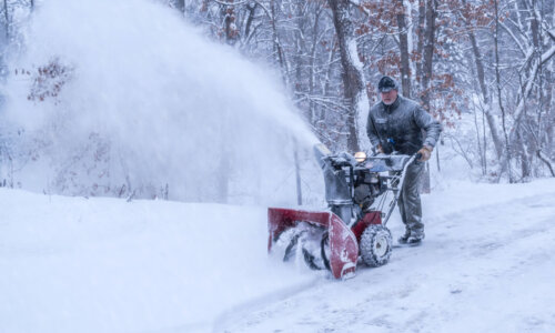 An old white man is using snow blower to plow / blow snow