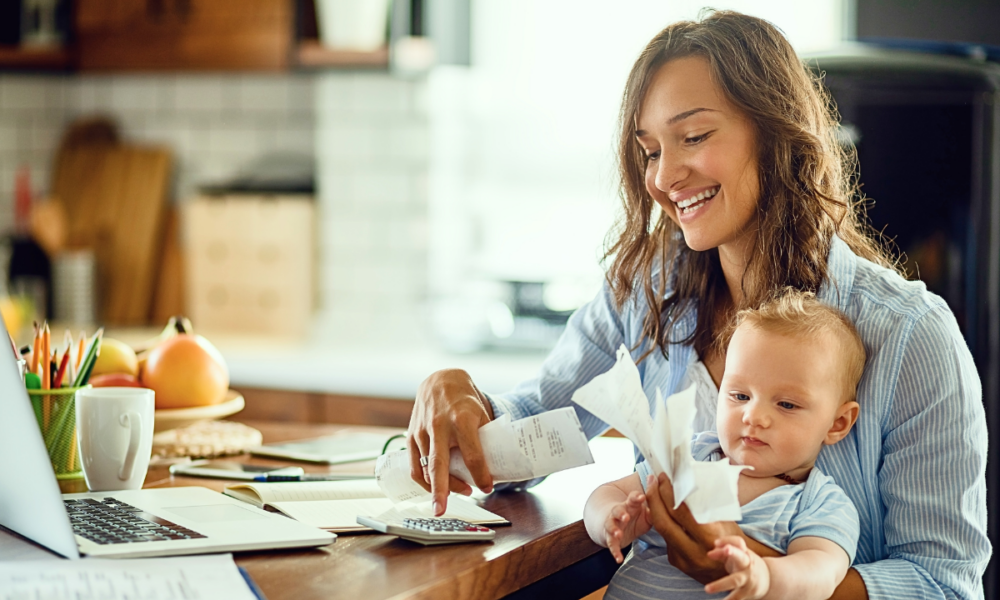 Smiling woman sitting at kitchen table with baby on lap while budgeting