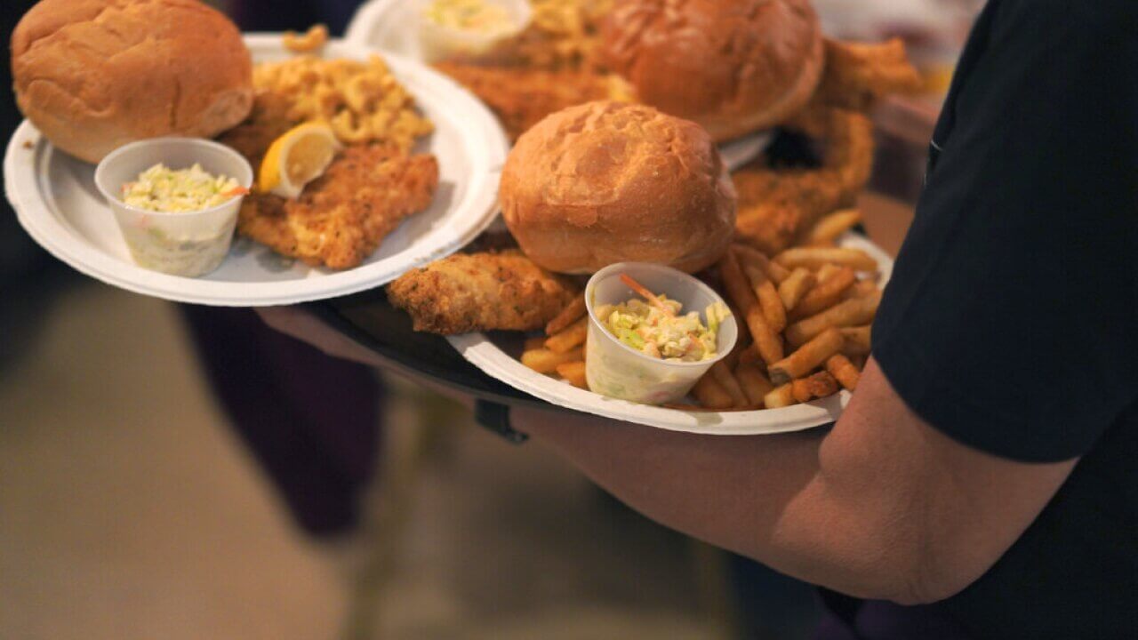 Person carries plates of fried fish sandwiches